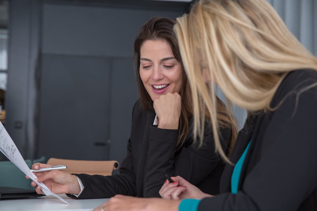 Two professional women discussing documents at an office meeting, showcasing teamwork and partnership.